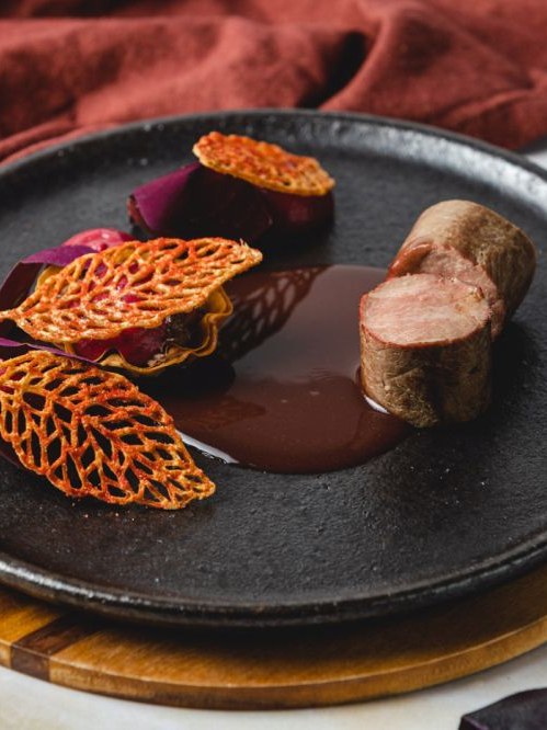 Plato de autor con tejas crujientes y salsa sobre plato de piedra